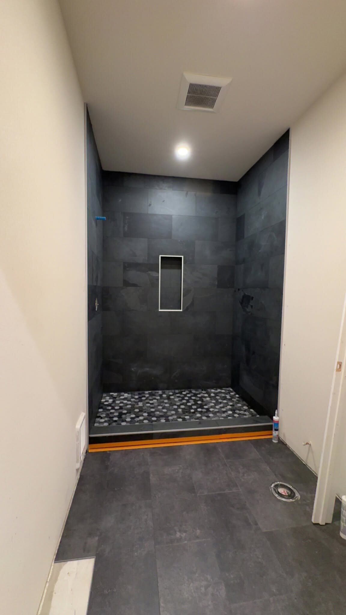 Dark tile walk-in shower with pebble floor installed by MG Flooring